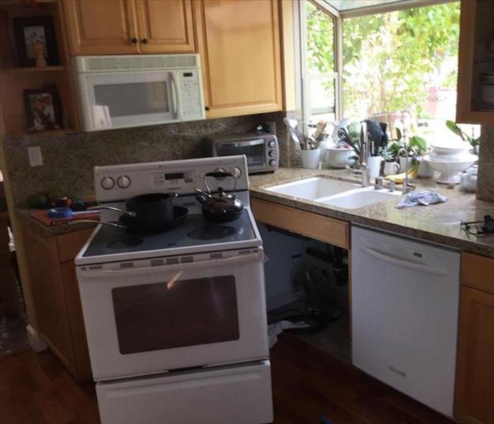 Image of kitchen with water damaged and white stove moved out of place in order to assess and treat water damaged surfaces.