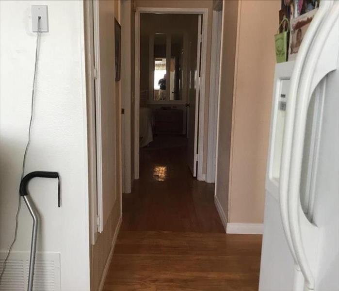 Image of small hallway leading to bedrooms and a bathroom with wood floors that are water damaged 