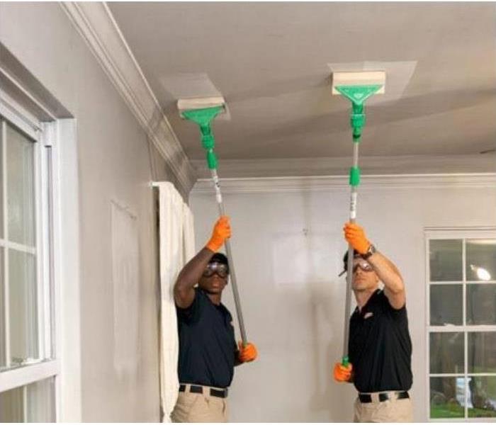 2 men cleaning a ceiling wall with smoke soot 